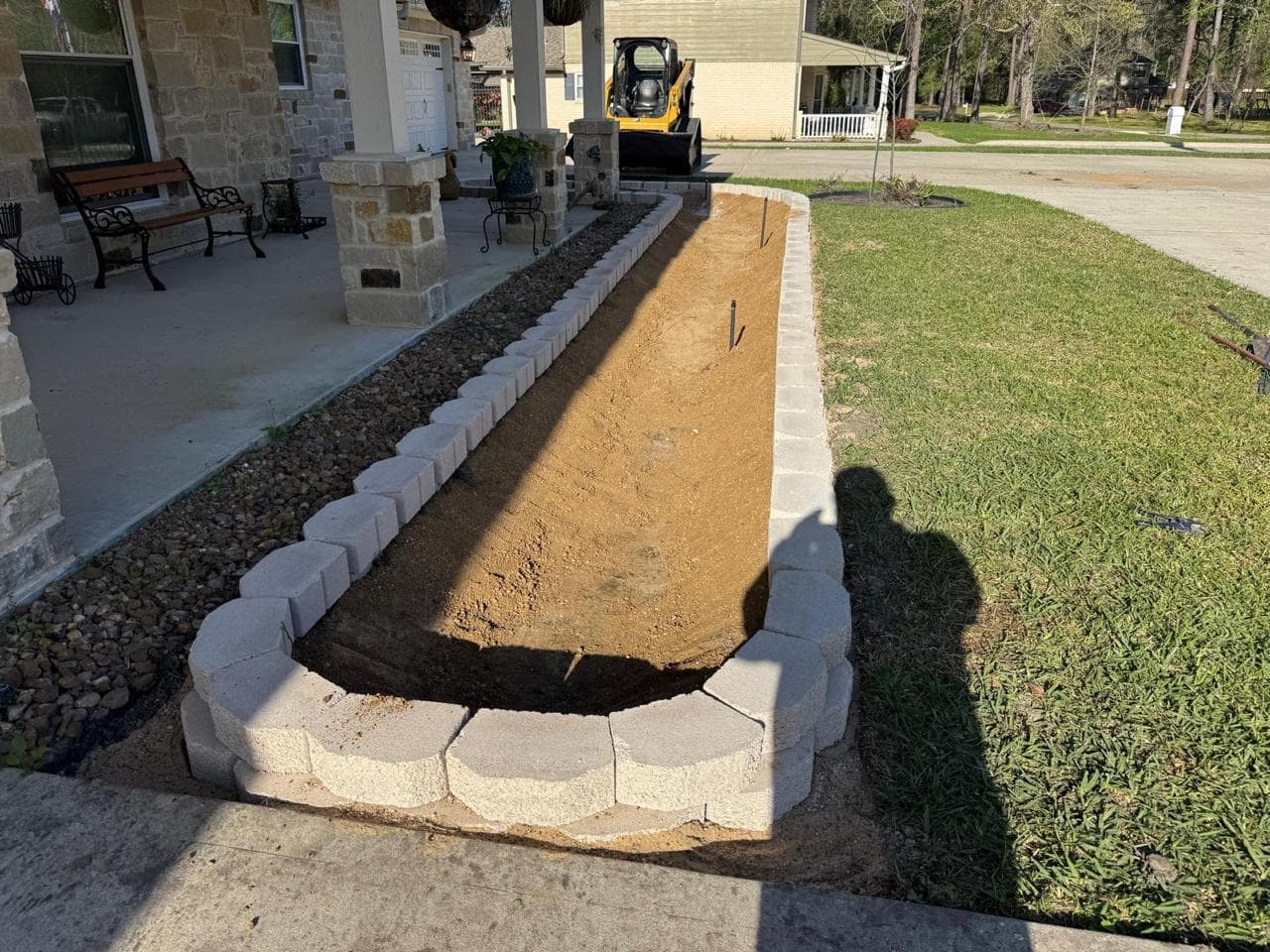Raised block-edged bed built along a front porch and backfilled with soil, ready for planting